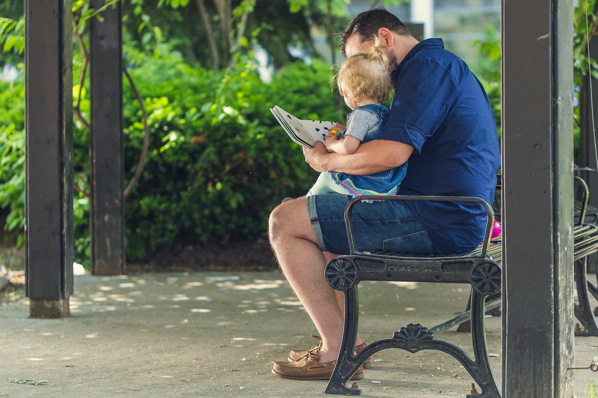 Father reading to his daughter on a park bench